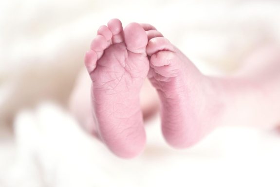 Zwei zarte Babyfüße auf einem weißen, weichen Hintergrund.