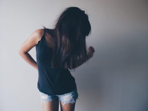Frau mit langen Haaren in einem schwarzen Top und Jeanskurzshorts, von hinten gesehen.